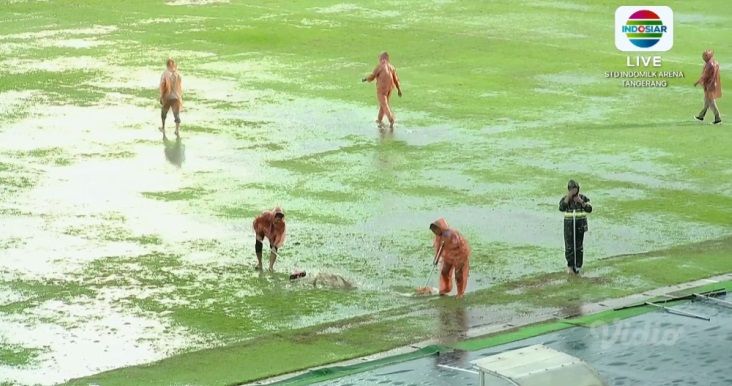 Petugas Indomilk Arena berupaya menyapu genangan air saat hujan deras mengguyur di laga Dewa United vs Bali United, 8 Desember 2023
